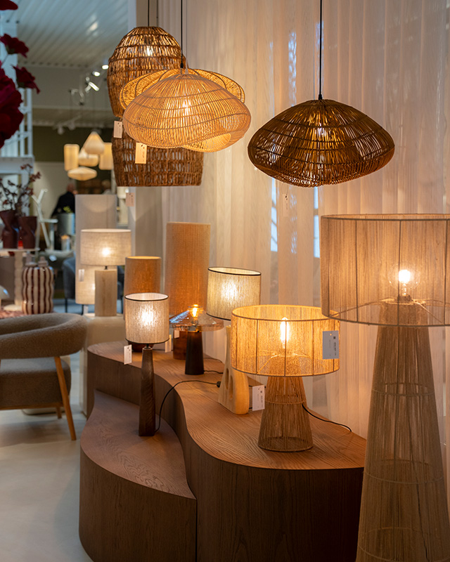 Houten presentatiemeubel met verschillende tafellampen erop en hanglampen erboven in showroom.